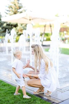 Young mother playing with little baby outside near fountain. Concept of walking in city and motherhood.