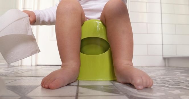 Funny baby boy sitting on chamberpot, Children's legs hanging down from a chamber-pot. Kid plays toilet paper