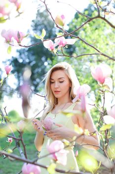 Young caucasian girl standing near magnolia in park. Concept of spring seasonal and nature.