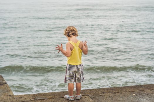 Cute boy stands on the shore watching the ocean waves.