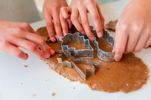 Kid's hands making gingerbread, cutting cookies of gingerbread dough. Christmas bakery. Friends making gingerbread view from above. Festive food, cooking process, family culinary, Christmas and New Year traditions concept