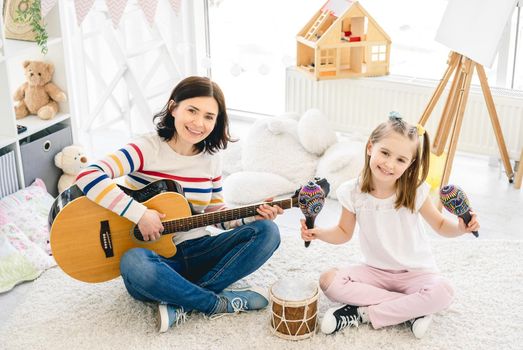 Nice little girl and mother playing musical instruments in kids room