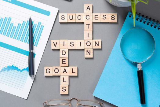 Business motivation concept with words from cubes. Still life of office workplace with crossword. Flat lay grey surface with magnifier and cup of coffee. New strategy planning and management