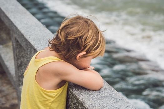 Cute boy stands on the shore watching the ocean waves.