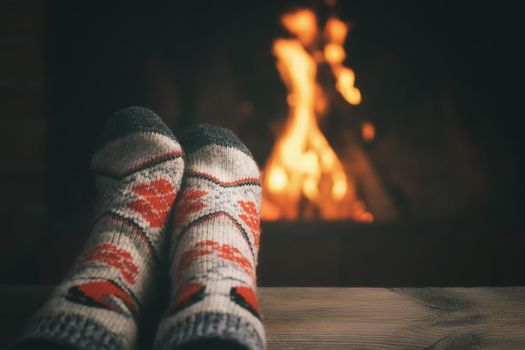 Girl resting and warming her feet by a burning fireplace in a country house on a winter evening. Selective focus.