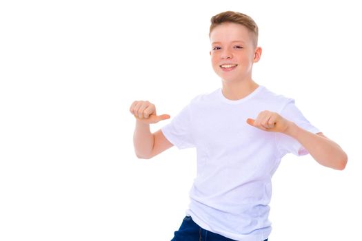A school-age boy points his fingers at his white T-shirt, on which you can make any inscription. The concept of advertising products, clothing design. Isolated on white background.