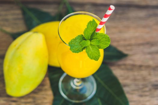 Juicy smoothie from mango in glass with striped red straw and with a mint leaf on old wooden background. Healthy life concept, copy space.