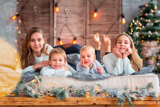 Happy kids siblings having fun on the bed near the Christmas tree on Christmas morning. Christmas family morning, christmas mood concept