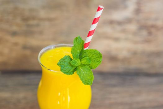 Juicy smoothie from mango in glass with striped red straw and with a mint leaf on old wooden background. Healthy life concept, copy space.