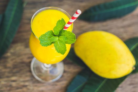 Juicy smoothie from mango in glass with striped red straw and with a mint leaf on old wooden background. Healthy life concept, copy space.