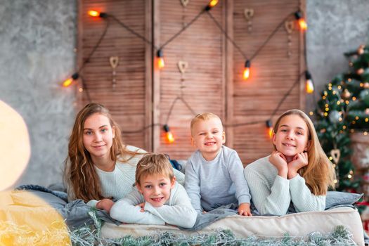 Happy kids siblings having fun on the bed near the Christmas tree on Christmas morning. Christmas family morning, christmas mood concept