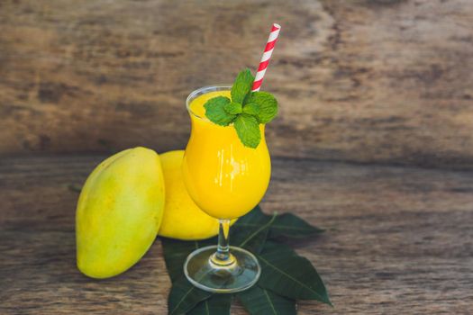 Juicy smoothie from mango in glass with striped red straw and with a mint leaf on old wooden background. Healthy life concept, copy space.