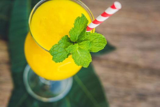 Juicy smoothie from mango in glass with striped red straw and with a mint leaf on old wooden background. Healthy life concept, copy space.