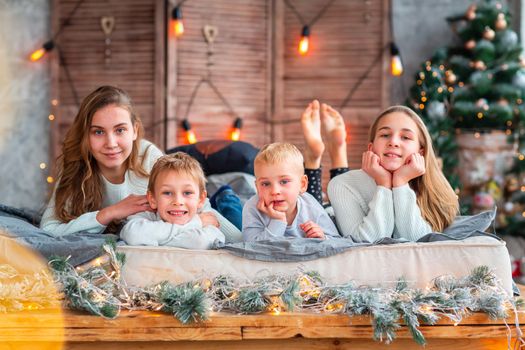 Happy kids siblings having fun on the bed near the Christmas tree on Christmas morning. Christmas family morning, christmas mood concept