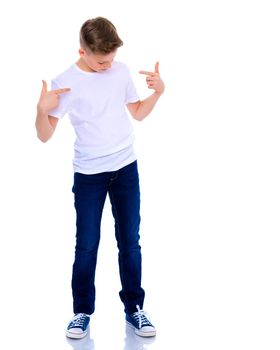 A school-age boy points his fingers at his white T-shirt, on which you can make any inscription. The concept of advertising products, clothing design. Isolated on white background.