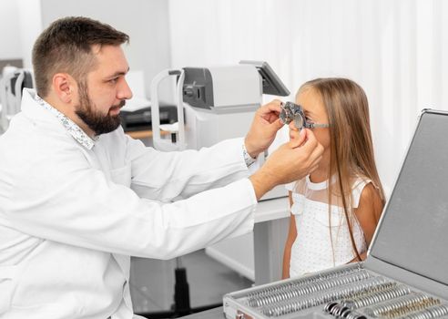 Doctor ophthalmologist holding special eye equipment examinating girl's eyes in the clinic