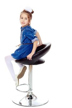 The little blonde girl with a large white bow on the head and short denim dress.She poses on a revolving chair.Isolated on white background.