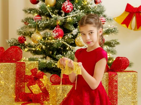 Beautiful little girl near the Christmas tree holds jewelry in her hands. Christmas concept new year.