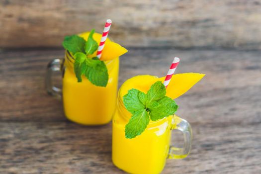 Juicy smoothie from mango in two glass mason jars with striped red straw on old wooden background. Healthy life concept, copy space.