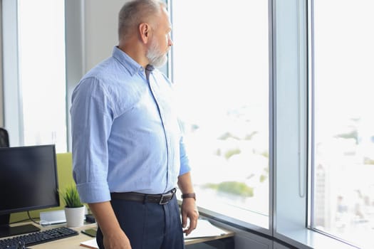 Thoughtful mature business man in a corporate suit looking away while standing near the window