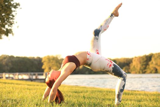 Concentrated pretty strong young redhead sports woman make yoga exercise outdoors