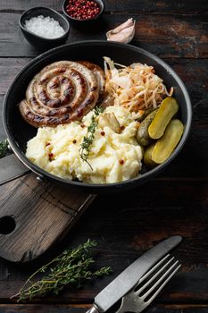 Fried Bavarian German Nürnberger sausages with sauerkraut, mashed potatoe in cast iron frying pan, on old dark wooden table background