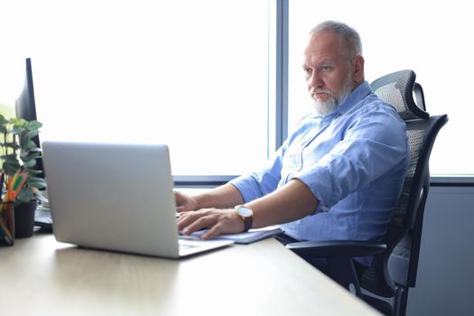 Senior businessman with a stylish short beard working on laptop computer at his office desk