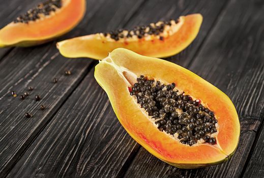 Several pieces of ripe papaya on a wooden table. Quarters of papaya on a dark plank table.