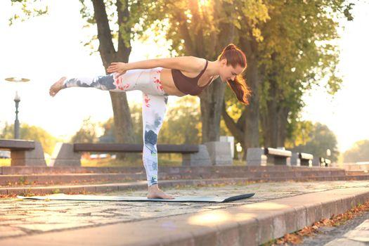 Athletic girl is doing advanced yoga asana on the fitness mat outdoors