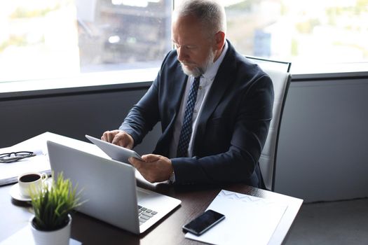 Mature business man in full suit using digital tablet while sitting in the office