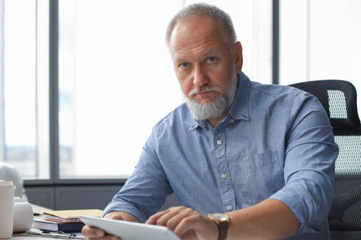 Mature businessman working using digital tablet while sitting in the modern office