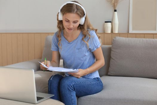 Smiling girl sit near couch watching webinar on laptop. Happy young woman study on online distant course