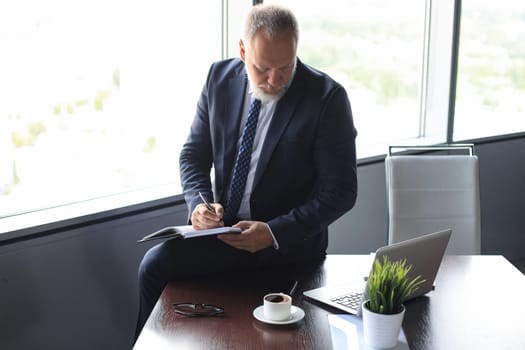 Focused mature businessman working and taking notes in his modern office
