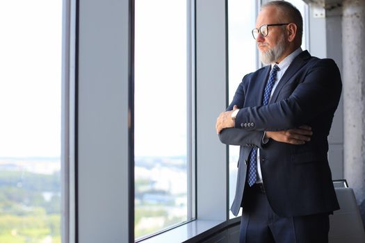 Thoughtful mature business man in full suit looking away while standing near the window