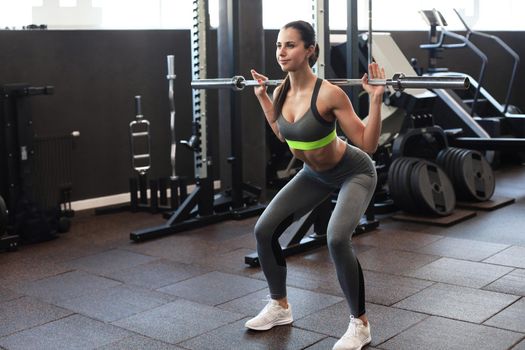 Muscular woman working out in gym doing exercises with barbell at biceps