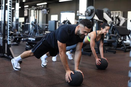 Beautiful young sports couple is working out with medicine ball in gym