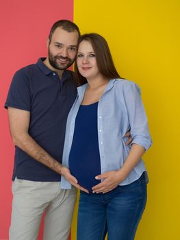 Portrait of a happy young couple,man holding his pregnant wife belly isolated over colorful background