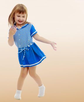 On a brown background a smooth transition from dark to light. Gentle little girl in a short blue dress similar to a sailor suit, with pleasure poses for the camera.