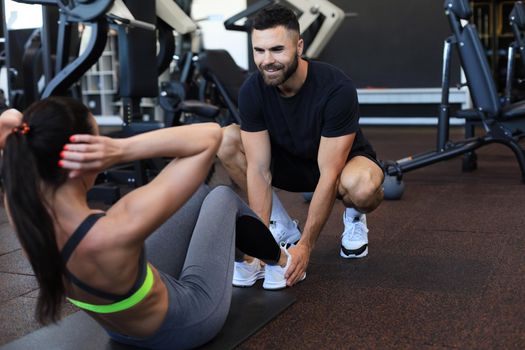 Trainer helping young woman to do abdominal exercises in gym