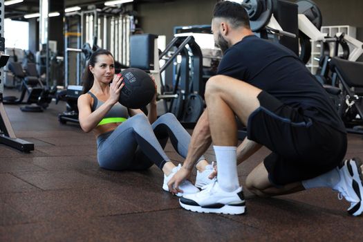 Trainer helping young woman to do abdominal exercises in gym