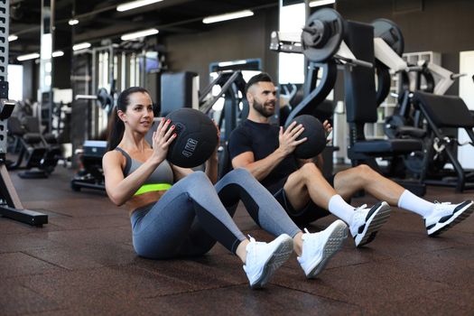 Beautiful young sports couple is working out with medicine ball in gym