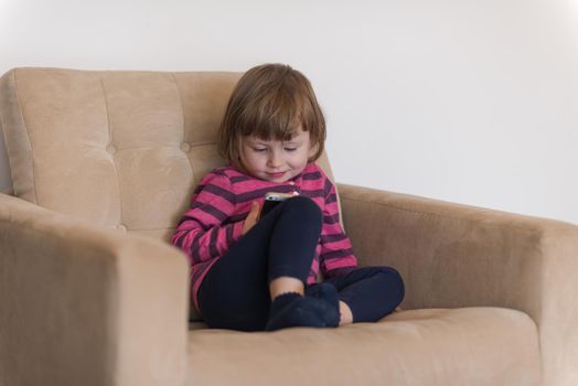 Portrait of cute little girl playing games on smartphone at home