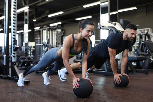 Beautiful young sports couple is working out with medicine ball in gym