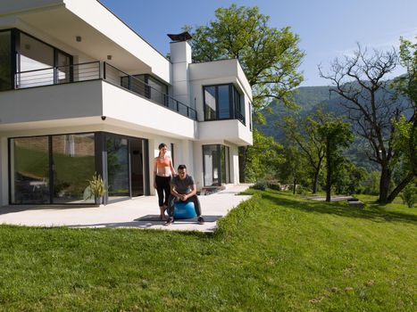 young beautiful woman and personal trainer doing exercise with pilates ball in front of her luxury home