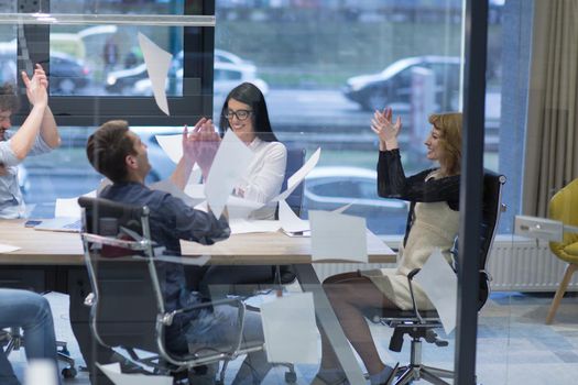 Group of young business people throwing documents and looking happy while celebrating success at their working places in startup office