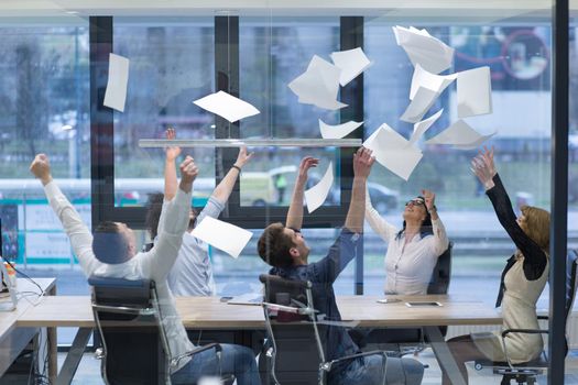 Group of young business people throwing documents and looking happy while celebrating success at their working places in startup office