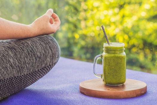 Closeup of a woman's hands during meditation with a green smoothies of spinach, orange and banana.