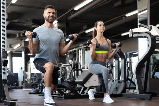 Attractive sports people are working out with dumbbells at gym