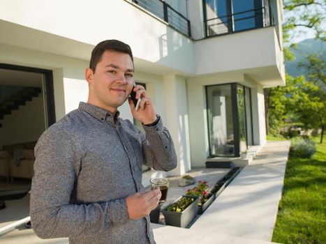 young handsome successful man using mobile phone in front of his luxury home villa