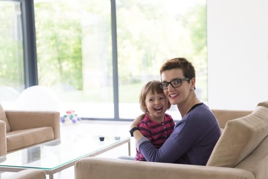 young mother and cute little girl enjoying their free time hugging on the sofa in their luxury home villa